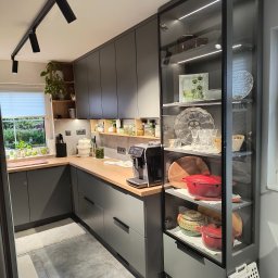 Project ZAZA - Nowoczesna kuchnia w odcieniach szarości z drewnianym blatem, oświetleniem punktowym i przeszkloną witryną z dekoracyjną zastawą.