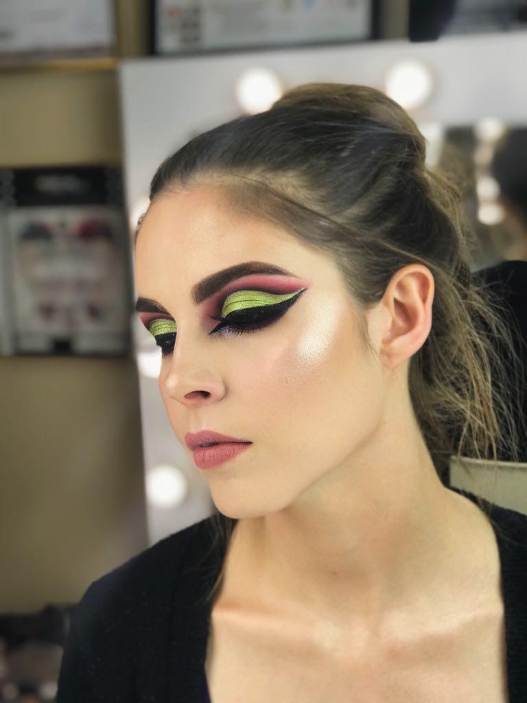 Profil kobiety z intensywnym makijażem oczu: zielony i różowy cień, mocna czarna kreska, rozświetlona skóra, upięte włosy.