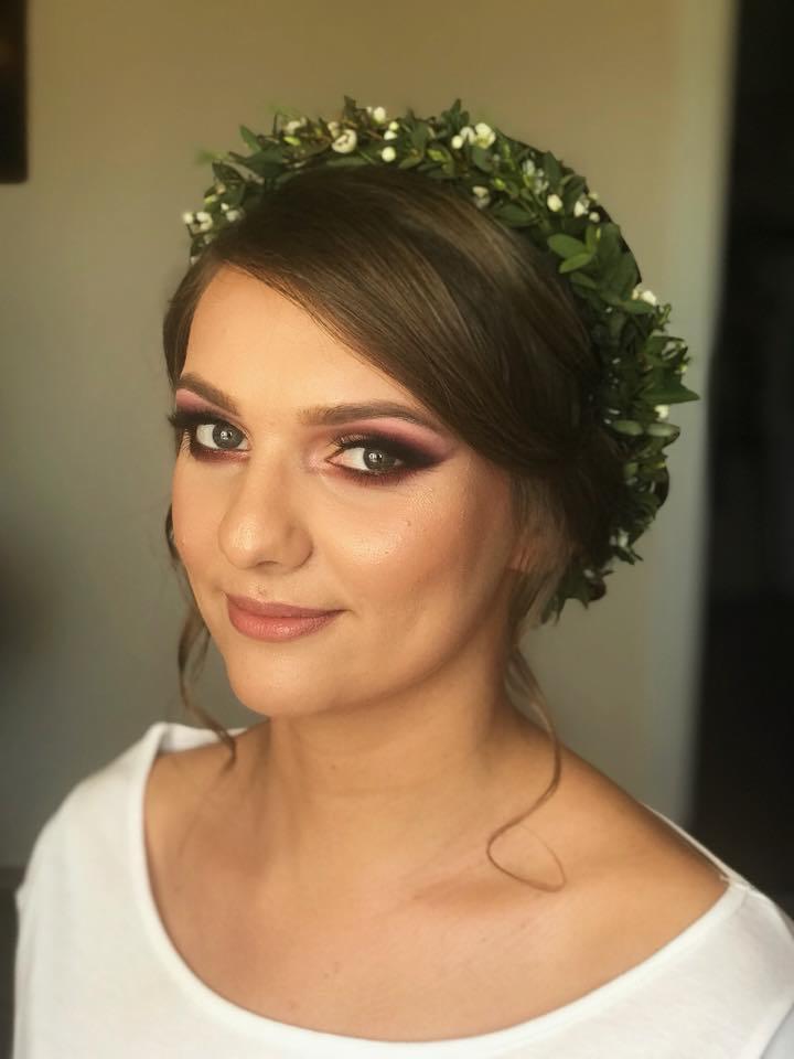 Portret kobiety z profesjonalnym, wieczorowym w fioletowych tonacjach i zielonym wiankiem na głowie, delikatny uśmiech, jasna karnacja.