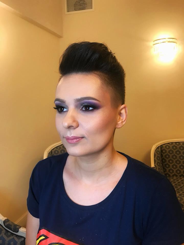 Portret kobiety z profesjonalnym, fioletowym makijażem oczu i delikatnym różem na policzkach, krótko ostrzyżone włosy z uniesioną grzywką.