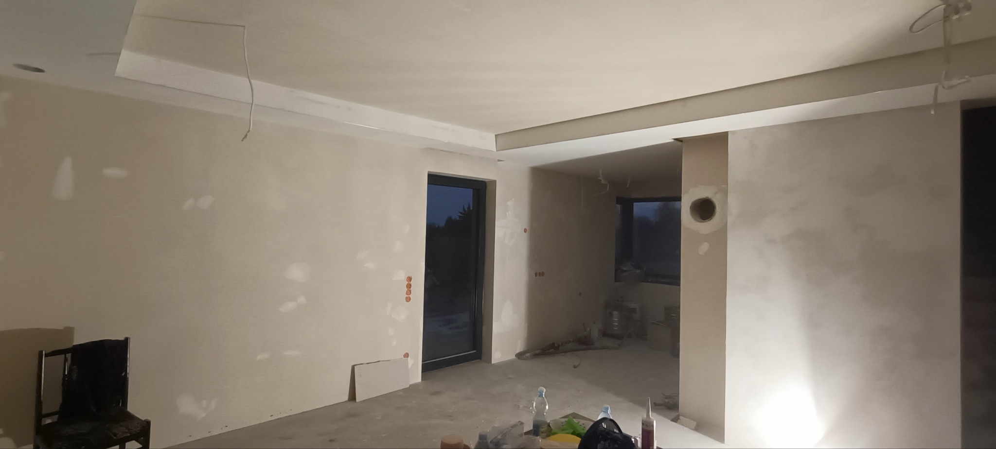 Pokój w trakcie prac wykończeniowych, ściany po szpachlowaniu, widoczne niedoskonałości i przygotowanie do dalszych etapów, w tle okno i elementy wyposażenia.