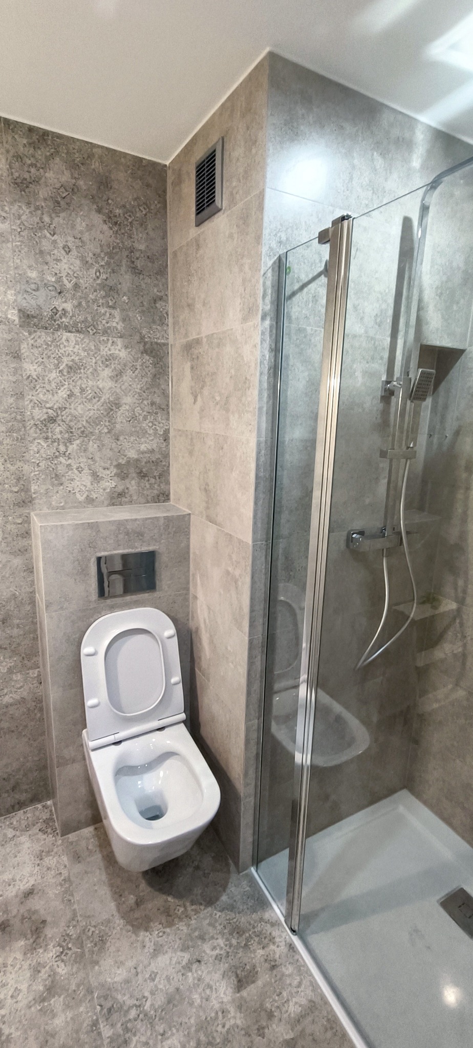 Nowoczesna łazienka z szarą mozaiką, podwieszana toaleta i przeszklona kabina prysznicowa z chromowaną armaturą.