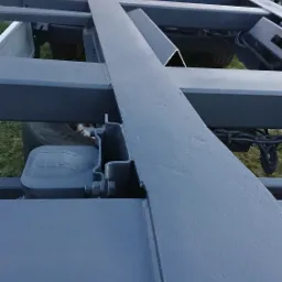 Metalowa rama przyczepy po piaskowaniu i malowaniu proszkowym w kolorze szarym, widoczne detale konstrukcyjne i elementy mocujące.