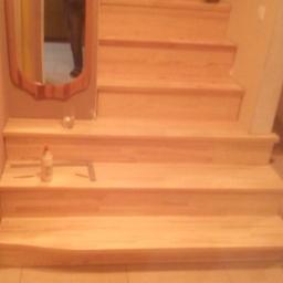 Uslugi Stolarskie Marcin Kanka - Jasne, drewniane schody w trakcie montażu, widoczne narzędzia i akcesoria, lustro z odbiciem osoby na ścianie.