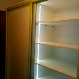 Wnętrze szafy wnękowej z przesuwnymi drzwiami, oświetlone pionowymi paskami LED, widoczne puste półki.