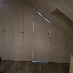 Uslugi Stolarskie Marcin Kanka - Biała zabudowa wnękowa pod skosem na poddaszu, widoczna twarz dziecka w lewym dolnym rogu, drewniana podłoga.