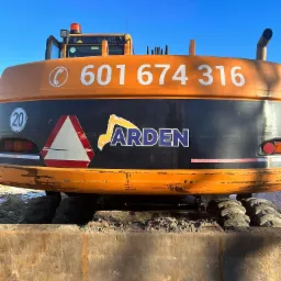 Pomarańczowa koparka z numerem telefonu 601 674 316 i logo 'ARDEN' na czarnym tle, widoczne opony i łyżka koparki, na boku znak ostrzegawczy i ograniczenie prędkości 20 km/h.