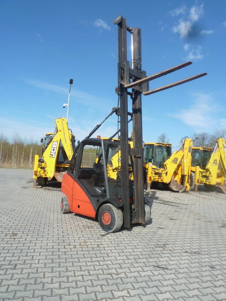 Pomarańczowo-czarny wózek widłowy z podniesionymi widłami na brukowanym placu, w tle żółte koparko-ładowarki i błękitne niebo.