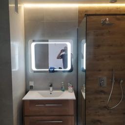 Sidbud - Nowoczesna łazienka z podświetlanym lustrem, kabiną prysznicową z drewnopodobnymi panelami i umywalką z szafką w odcieniach drewna.