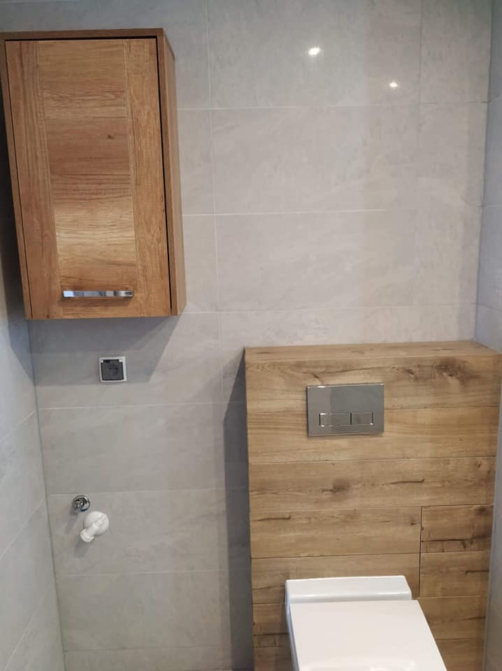 Nowoczesna łazienka z drewnianą zabudową geberitu i szafką wiszącą z jasnymi, kwadratowymi płytkami na ścianach.