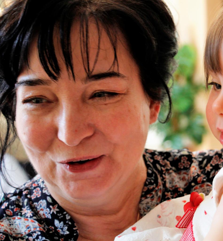 Uśmiechnięta kobieta z czarnymi włosami trzyma na rękach małe dziecko w Kaliszu.