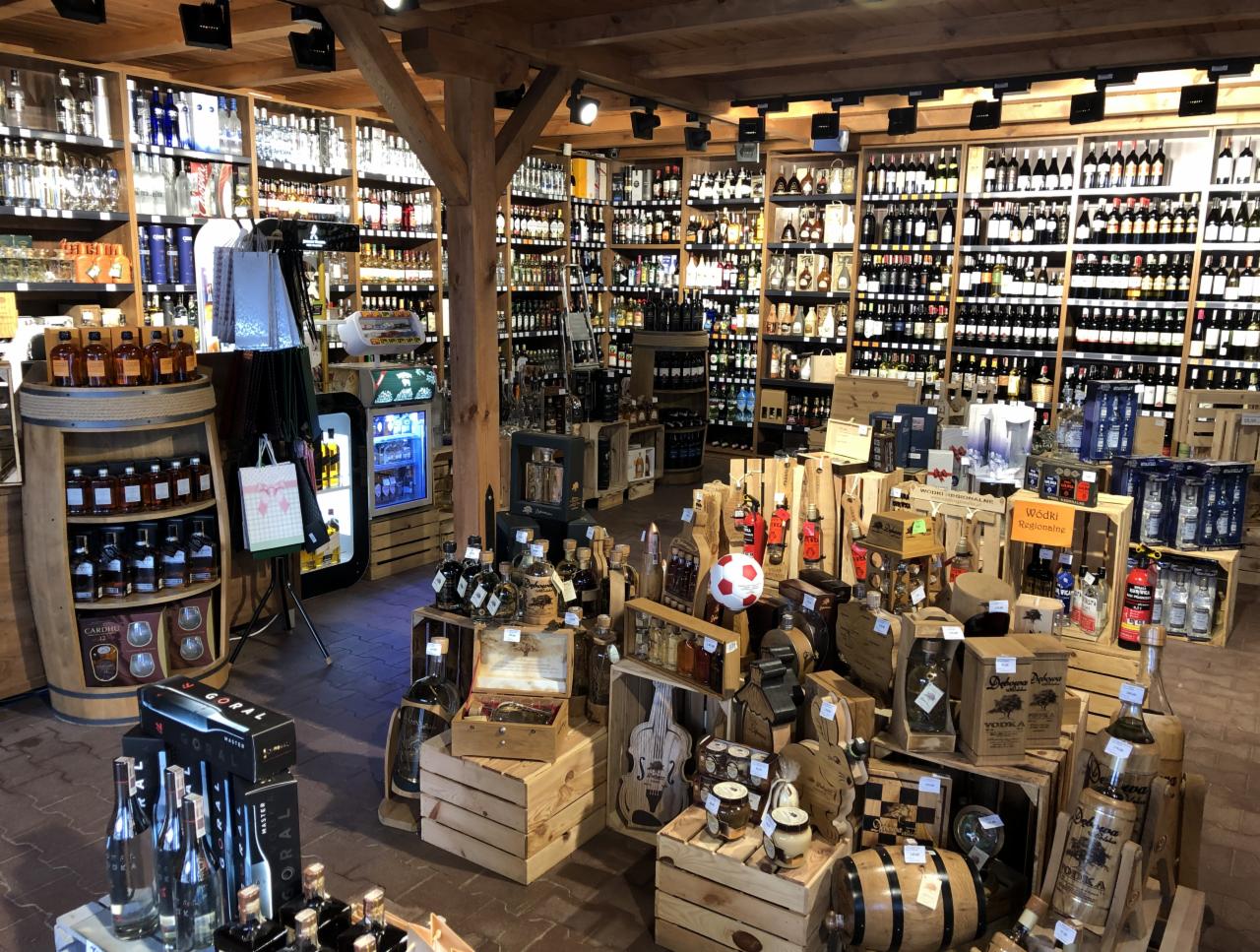 Wnętrze przestronnej hurtowni alkoholi z drewnianymi regałami wypełnionymi butelkami różnych trunków, ekspozycja na drewnianych skrzyniach z dekoracyjnymi elementami, w tym piłką do nogi.