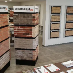 Ekspozycja różnych kolorów i faktur cegieł klinkierowych marki Vandersanden w salonie sprzedaży, z katalogami i próbkami na ścianie.