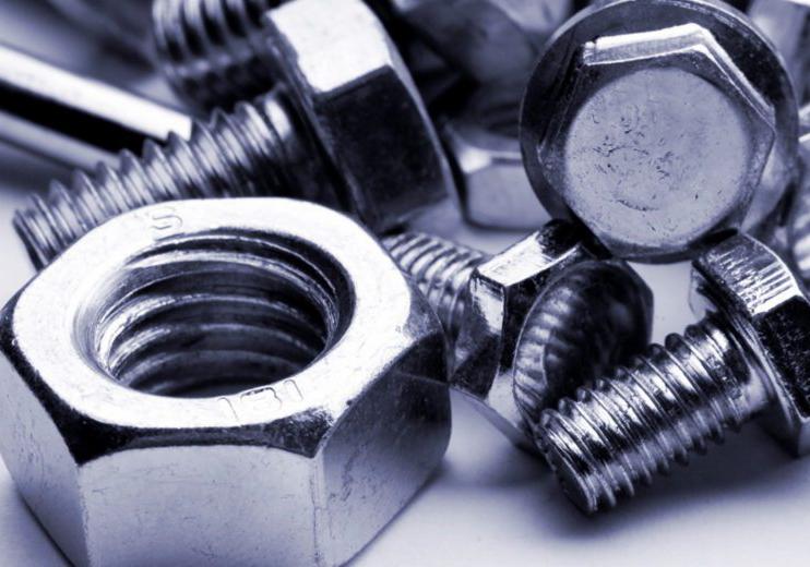 Makro zbliżenie na srebrne śruby i nakrętki o sześciokątnych łbach, widoczne gwinty i oznaczenia producenta na jednej z nakrętek, ułożone na białym tle.
