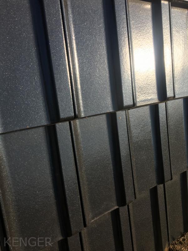 Szczegółowe zbliżenie na ułożone arkusze metalowej blachy trapezowej w kolorze grafitowym, z widocznym połyskiem odbitego światła słonecznego.