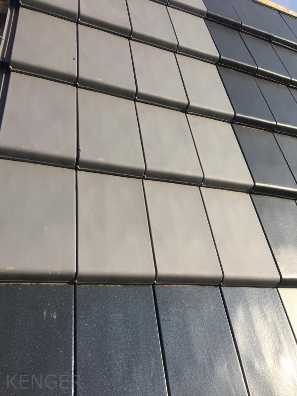 Szare, kwadratowe elementy pokrycia dachowego ułożone rzędami, widoczne z bliska pod kątem, dolne rzędy w odcieniu grafitowym, górne jaśniejsze, z widocznym znakiem wodnym 'KENGER'.