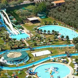 Widok z góry na park wodny z licznymi zjeżdżalniami, basenami, leniwą rzeką i palmami, otoczony zielenią drzew i krzewów.