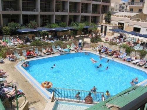 Widok z góry na hotelowy basen z błękitną wodą, otoczony leżakami i parasolami, gdzie relaksują się ludzie.