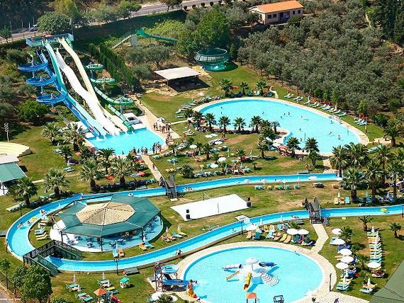 Widok z góry na park wodny z licznymi zjeżdżalniami, basenami, leniwą rzeką i palmami, otoczony zielenią drzew i krzewów.