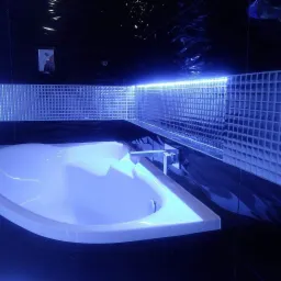 Nowoczesna łazienka z wanną, czarnymi płytkami i podświetlaną mozaiką szklaną nad wanną, oświetlenie LED.