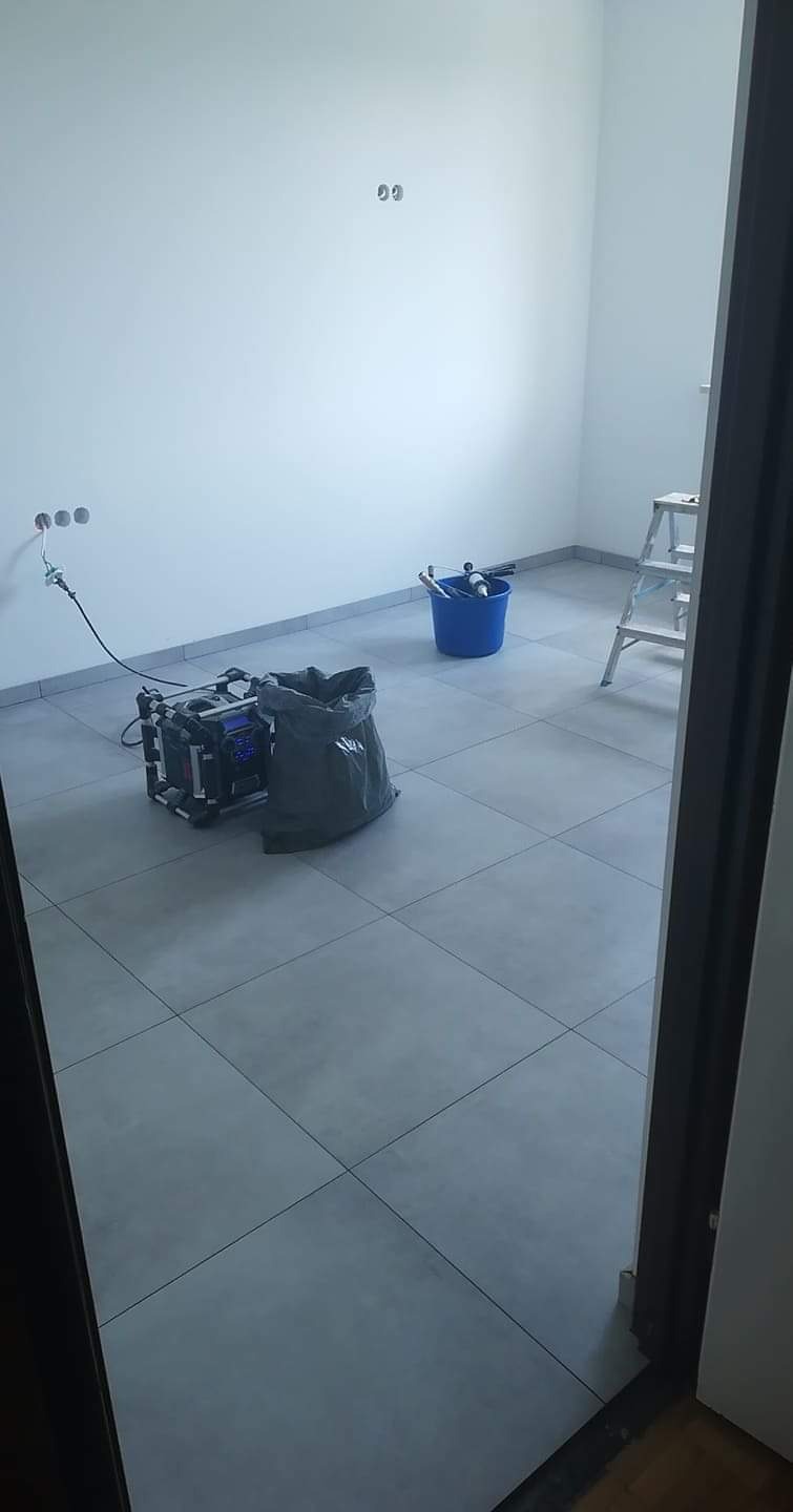 Północno-zachodni kadr z wnętrza pokoju po niedawnym odświeżeniu ścian, z widocznym agregatem malarskim podłączonym do gniazdka, wiadrem z narzędziami malarskimi i workiem na śmieci, ustawionymi...