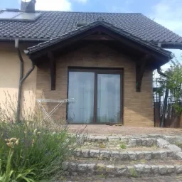 Dwukondygnacyjny budynek z brązowymi drzwiami balkonowymi, kamiennymi schodami i kwitnącą lawendą na pierwszym planie.