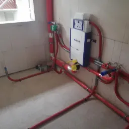 Wnętrze w trakcie instalacji hydraulicznej: czerwone rury rozprowadzone po podłodze i ścianach z zamontowanym stelażem podtynkowym WC marki Geberit.