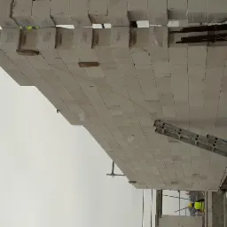 Wznoszenie stropu z bloczków betonowych na budowie, widoczna drabina i elementy konstrukcyjne.