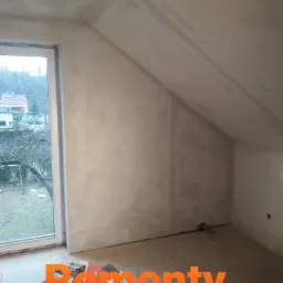 Poddasze w trakcie szpachlowania ścian i sufitu, widoczne worki z gładzią gipsową Śnieżka Euro-Gips, okno z widokiem na ogród.