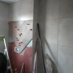 Układanie płytek na ścianie w łazience z użyciem klipsów poziomujących, widoczna drabina i narzędzia.