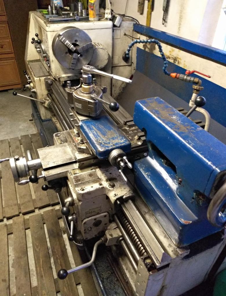 Używana tokarka z uchwytem tokarskim i narzędziem skrawającym, widoczna instalacja chłodzenia i narzędzia na obudowie.