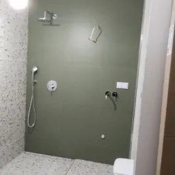 Nowoczesna łazienka w trakcie wykańczania, widoczne szare płytki, biała armatura, zamontowana deszczownica i bateria, zarys toalety, brakujące elementy wyposażenia.