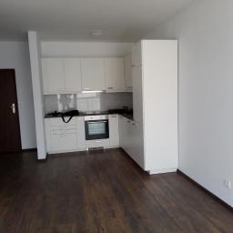 REN-BUD.WAW KRZYSZTOF GRAB - Wnętrze mieszkania po remoncie: ciemna podłoga z paneli, białe ściany i zabudowa kuchenna z białymi szafkami i sprzętami AGD.