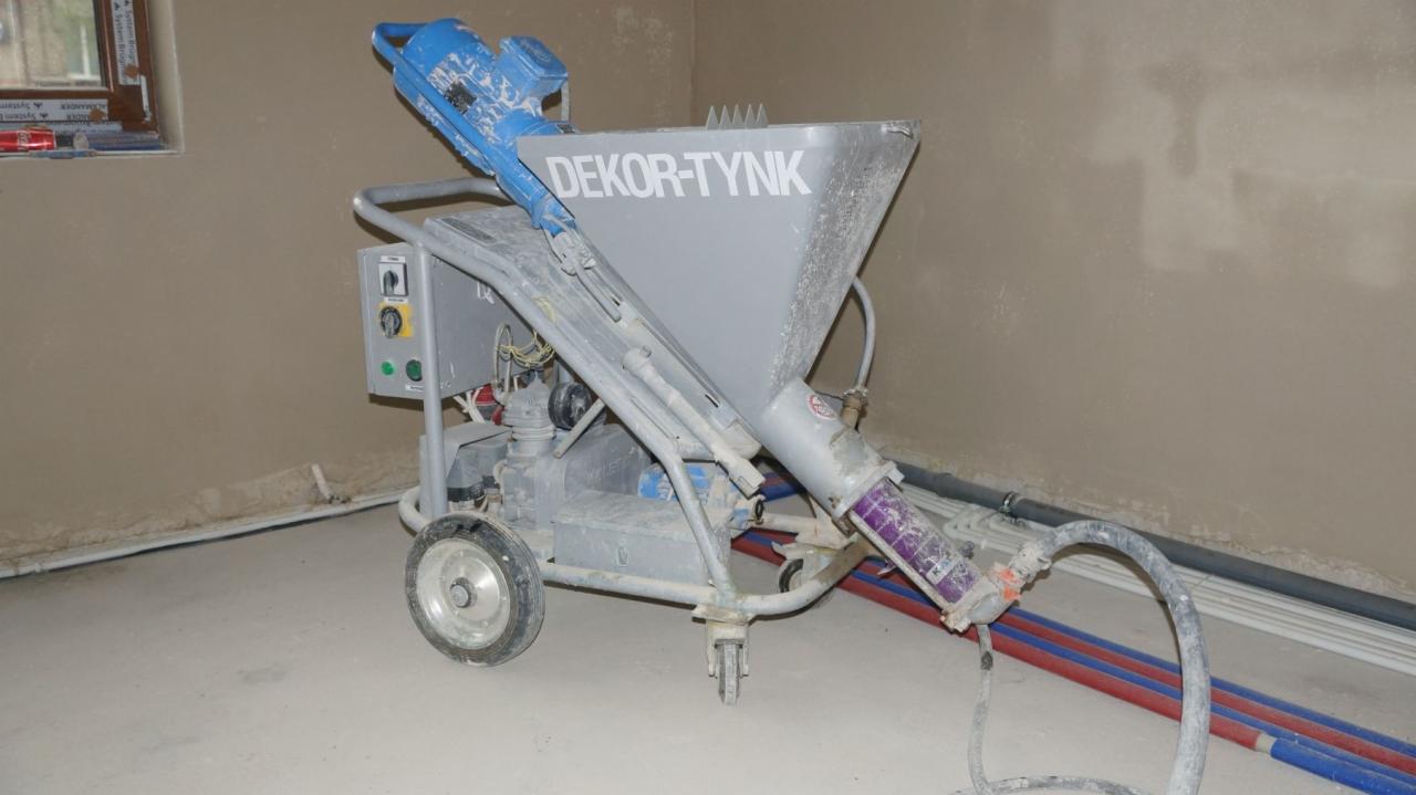 Agregat tynkarski marki Dekor-Tynk na kółkach, z widocznymi przewodami i świeżo otynkowaną ścianą w tle.