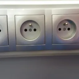 Szereg czterech szarych gniazdek elektrycznych typu francuskiego (Schuko) zamontowanych w listwie, widoczne bolce uziemiające i otwory na wtyczki.