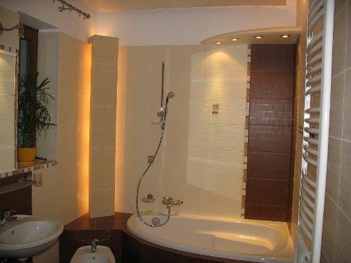 Jasna łazienka z wanną, bidetem i umywalką, oświetlona punktowo, z elementami dekoracyjnymi z płytek w odcieniach brązu i beżu.