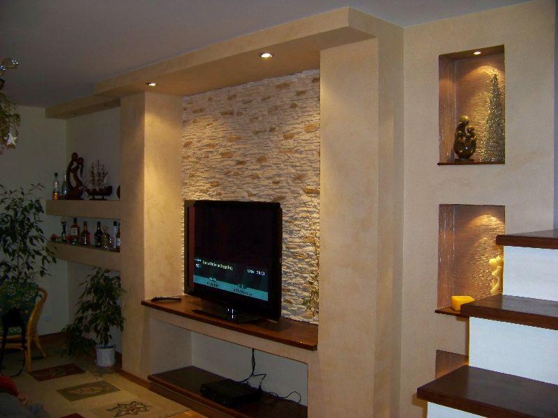 Salon z dekoracyjną ścianą z kamienia, wnękami z oświetleniem i półkami na alkohol, wykończony w odcieniach beżu i brązu.