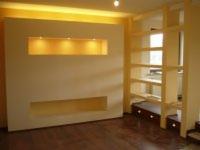 Salon z wnękami w ścianie podświetlonymi ciepłym światłem i drewnianym regałem z półkami.