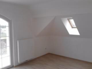 Poddasze z oknem dachowym po malowaniu na biało, widoczny grzejnik i panele podłogowe.