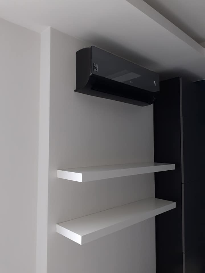 Czarny klimatyzator LG zamontowany na ścianie nad dwoma białymi półkami w nowoczesnym wnętrzu.