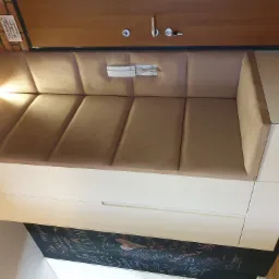 Beżowa, tapicerowana wnęka do siedzenia z białymi szafkami na dole, na ścianie domofon, obok ściana z cegły i tablica kredowa.