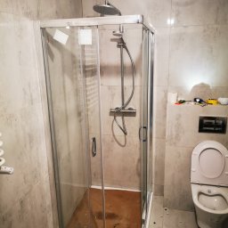 TIMWEK KATARZYNA KORBUT - Montaż kabiny prysznicowej z przesuwnymi drzwiami, widoczne narzędzia i płytki imitujące kamień w trakcie remontu łazienki.