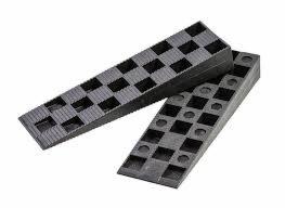 Dwa kliny poziomujące z tworzywa sztucznego, ułożone jeden na drugim, z wytłoczonym wzorem szachownicy z kwadratowymi otworami, na białym tle.