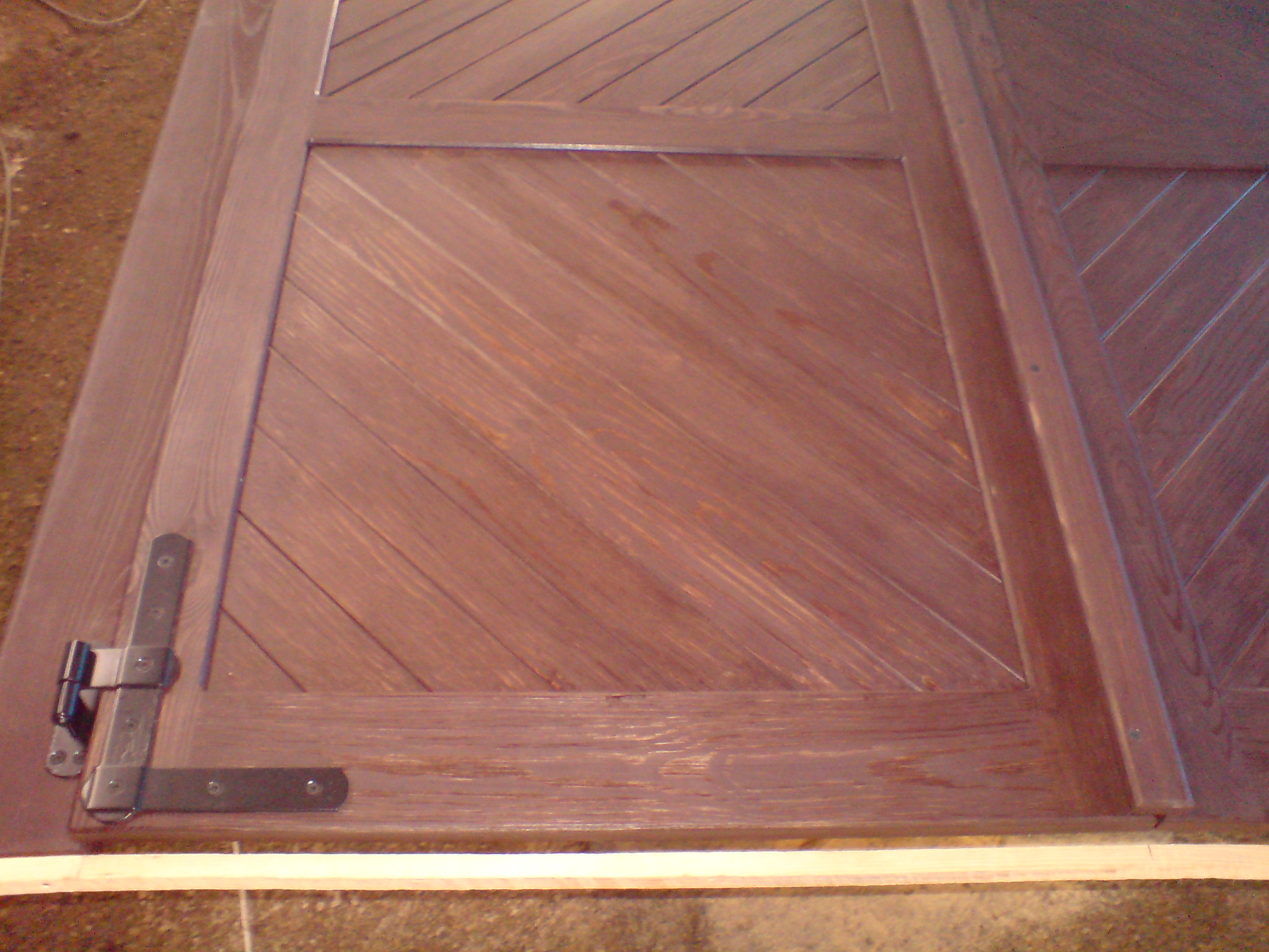 Ciemnobrązowe, drewniane okiennice z ukośnym wzorem i metalowymi zawiasami, leżące na podłodze.