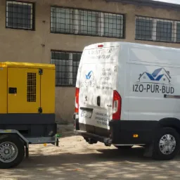 Żółty agregat prądotwórczy na przyczepie, biały samochód dostawczy z logo firmy IZO-PUR-BUD i dane kontaktowe, oraz mężczyzna w czarnej koszulce na tle budynku z kratami w oknach.