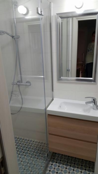 Nowoczesna łazienka z prysznicem za szklaną ścianką, umywalką w szafce z drewnianymi frontami i lustrem w srebrnej ramie, wzorzysta podłoga.