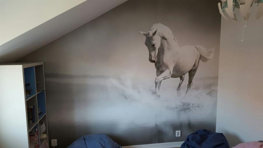 Fototapeta z białym koniem galopującym po wodzie, umieszczona na ścianie pokoju na poddaszu ze skosem, obok białego regału z niebieskimi wstawkami i wiszącej lampy.