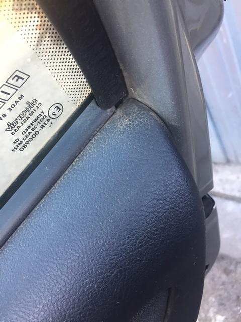 Szczegółowe zbliżenie na zabrudzoną, teksturowaną tapicerkę samochodową w rogu deski rozdzielczej przy przedniej szybie, widoczne osady kurzu i plamy.