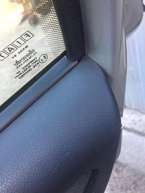 Fragment wnętrza samochodu marki FIAT, widoczna tapicerka drzwi w kolorze granatowym, uszczelka okienna i szyba z naklejkami informacyjnymi.