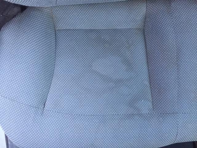 Fragment szarej tapicerki fotela z widocznymi plamami przed czyszczeniem.